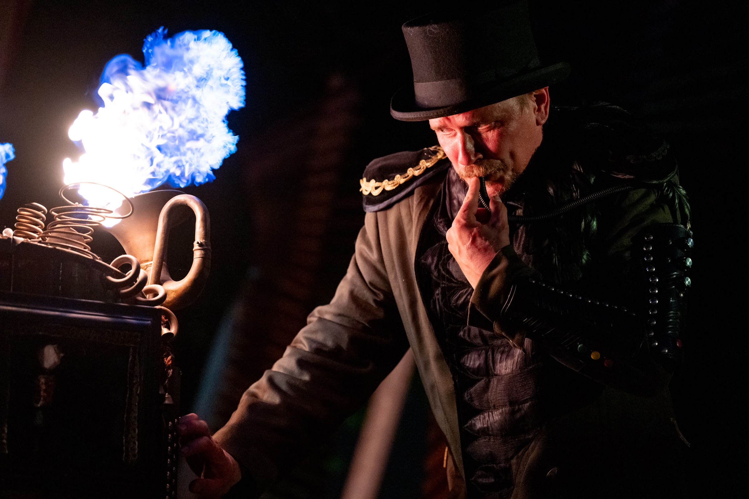Hjalte in a top hat and coat at Tromleorkestret's music machine, a blue flame rising beside him